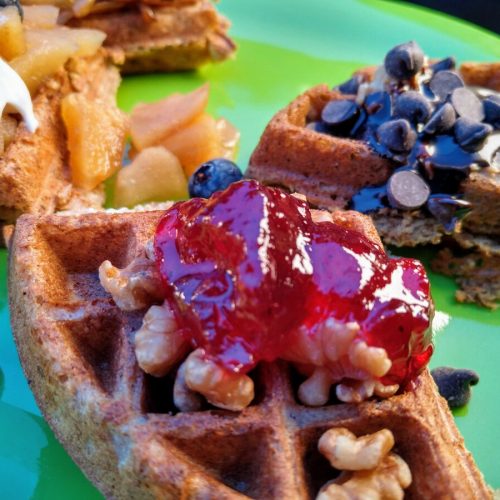 vegan waffle topped with walnuts, fruit jam, chocolate chips, blueberries, baked apples, and chocolate syrup
